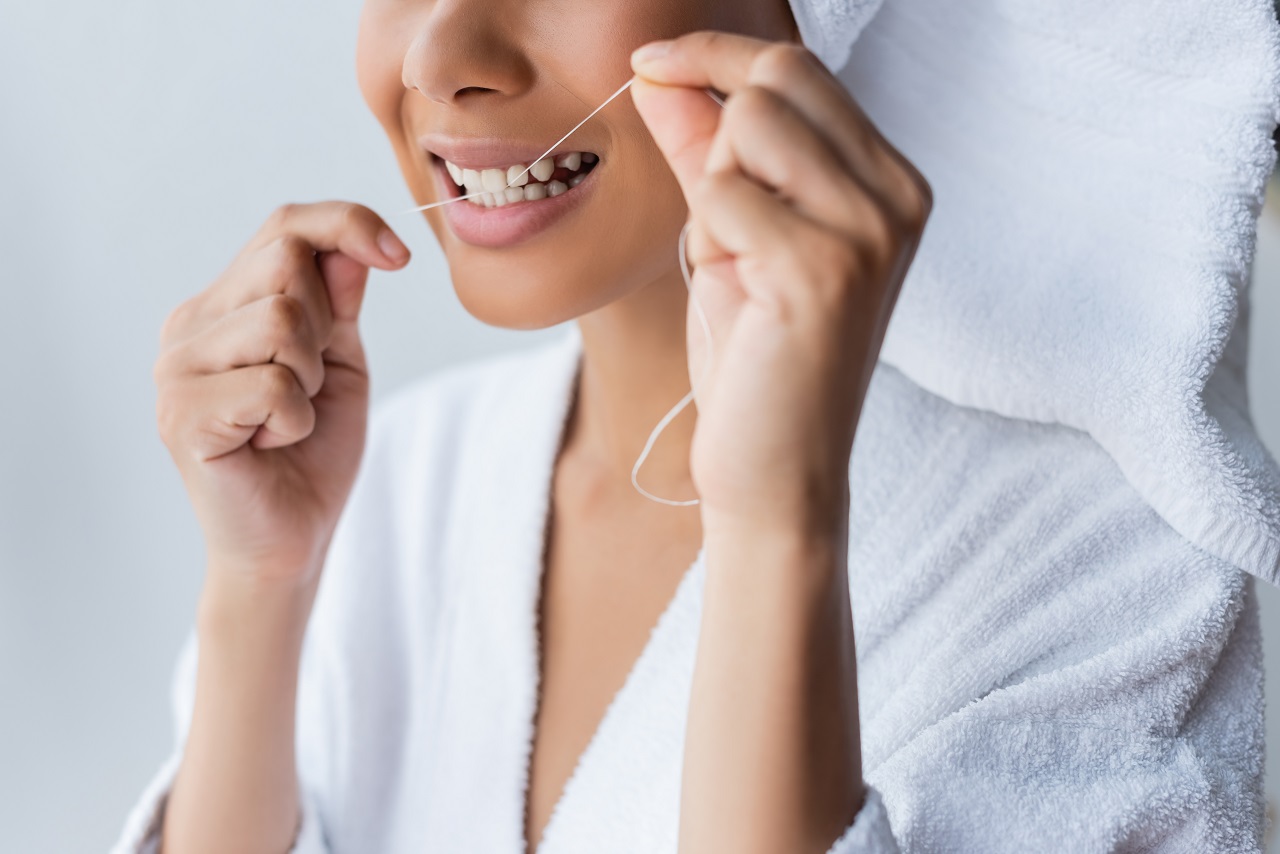 cropped view of smiling young african american woman in bathrobe flossing teeth in bathroom